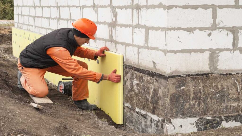 Expert installeert gevelisolatie onderaan de buitengevel.